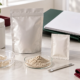 Conceptual formulation table with unbranded sample containers, pouch, capsule shells, powder dish, sachet mockup, mixing beaker, and blank project binder