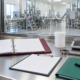 Conceptual audit station with blank evidence binder, checklist clipboard, sealed sample container, digital balance, sampling tool, and generic processing room