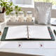 Conceptual ingredient project planning desk with binder, sample jars, sealed pouch, sequence cards, laptop, pen, and digital scale